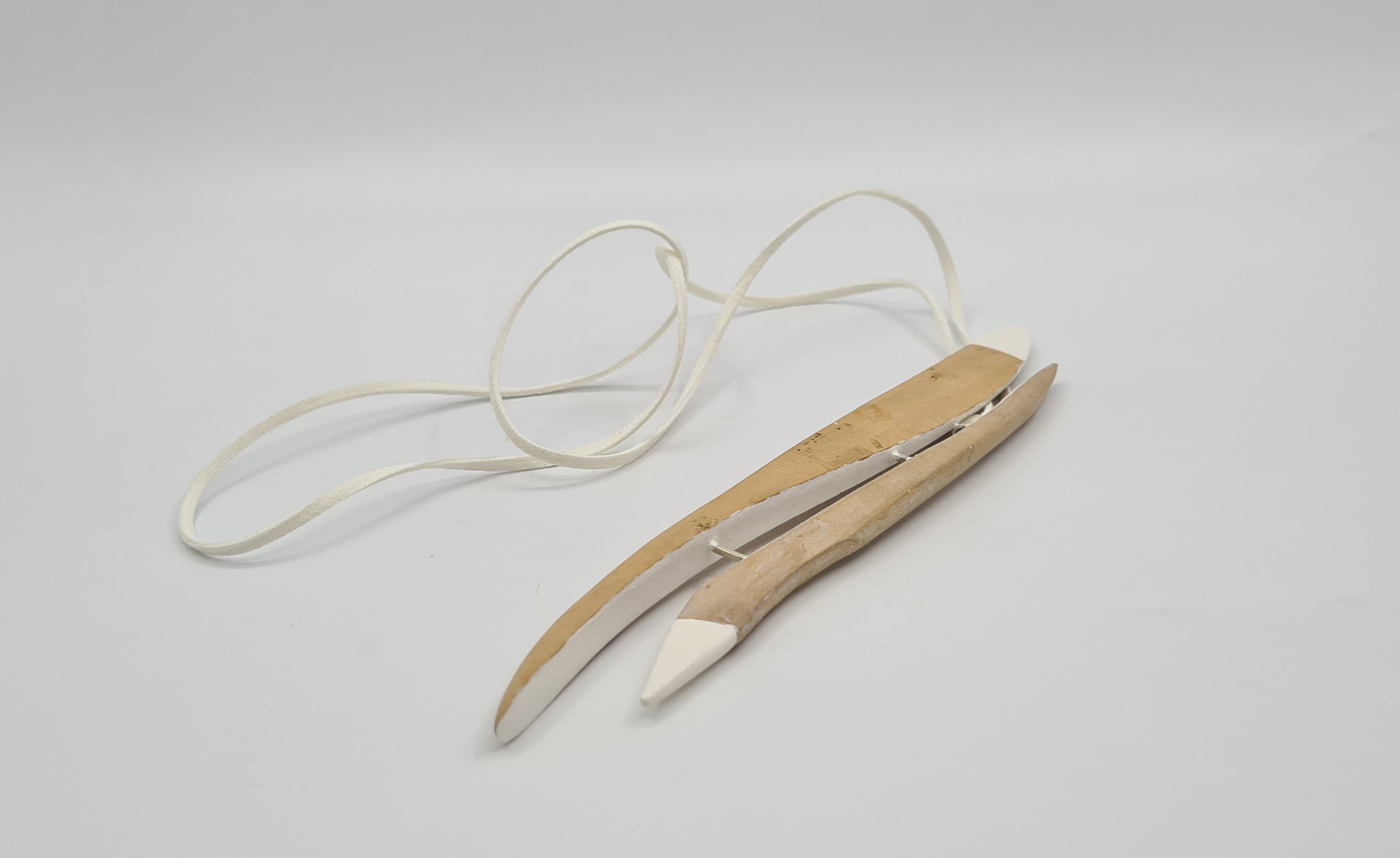 Long pendant of carved wood tipped with white porcelain, strung on a white suede cord.