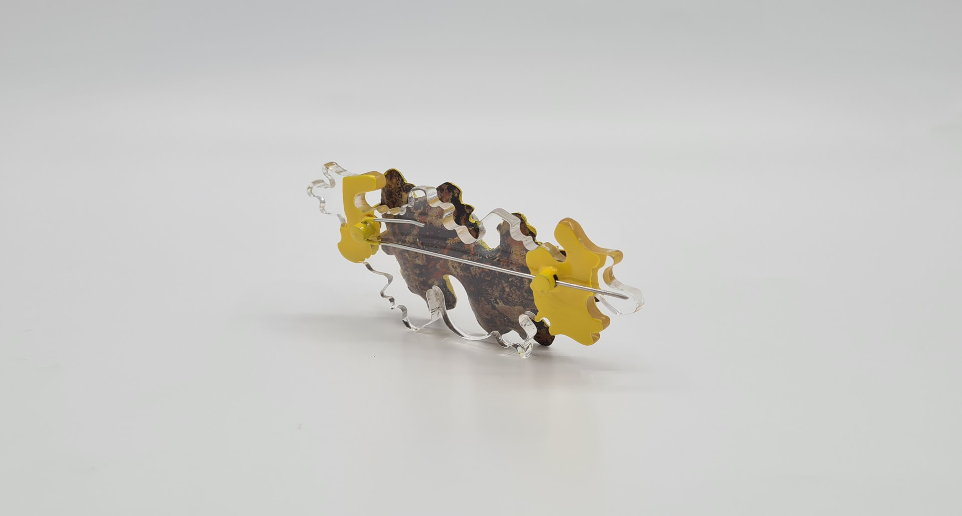 Brooch of layered clear and yellow acrylic over a rusted leaf-shaped element, with a silver pin.