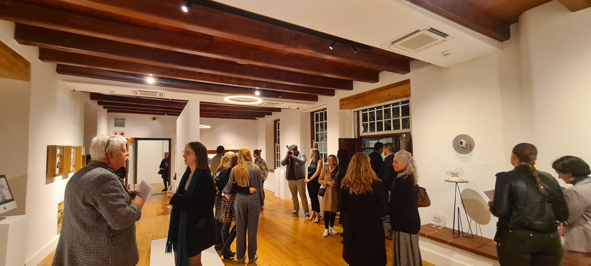 Opening night of TEN-SION at Oude Leeskamer Gallery — guests gathered among the art jewellery displays under exposed timber beams.
