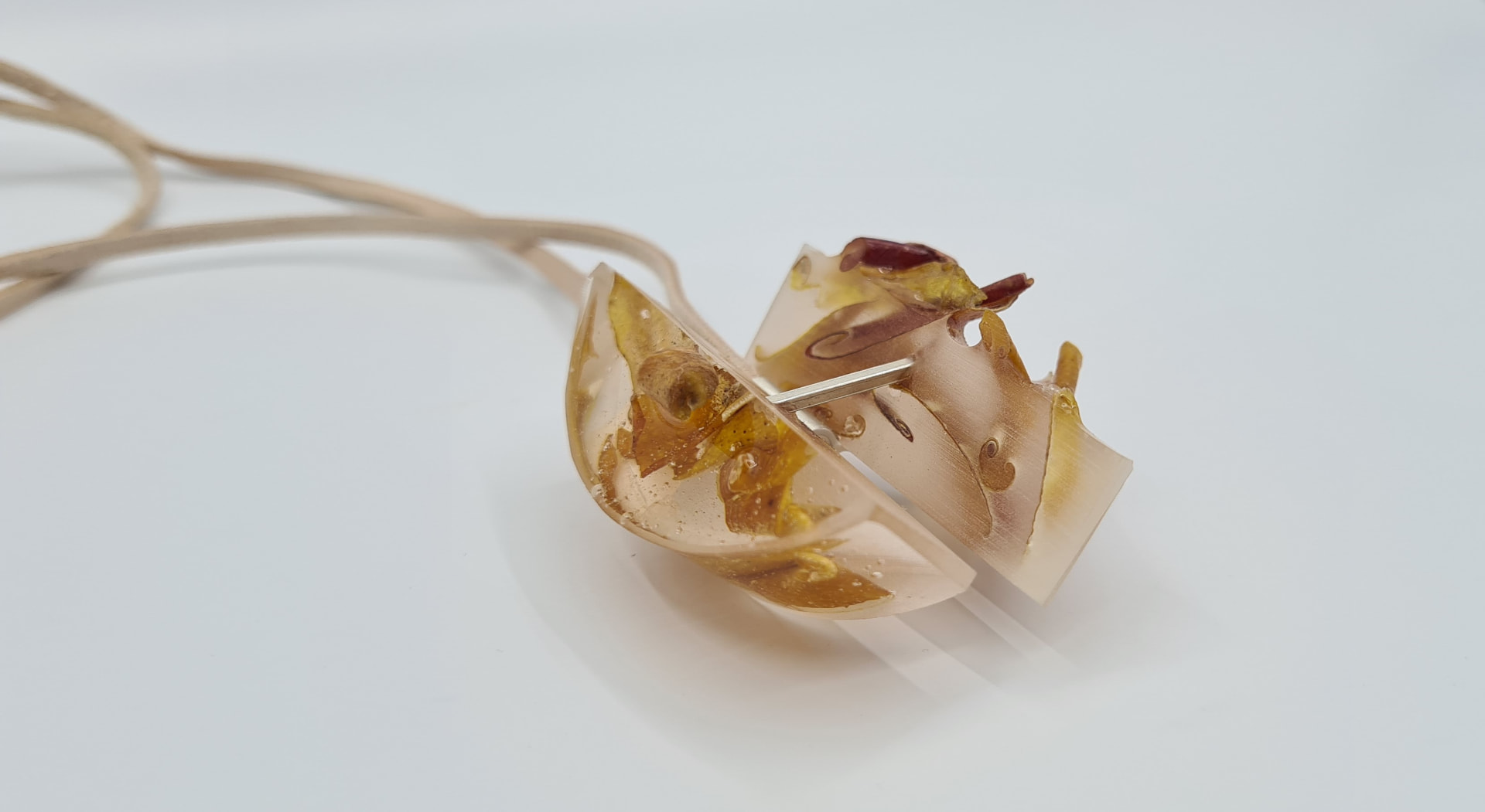 Pendant of translucent resin set with pressed golden petals on a natural suede cord.