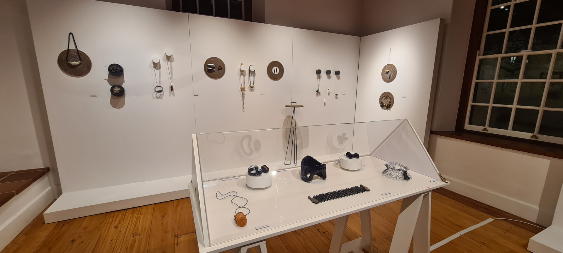 Install view of TEN-SION at Oude Leeskamer Gallery — wall-mounted art jewellery in porcelain, silver and steel above a vitrine of sculptural neckpieces.